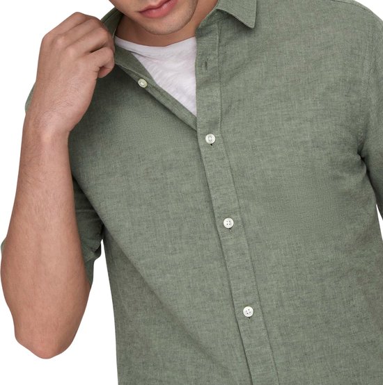 Detail van een groen, kortarmig hemd met witte knopen en een witte T-shirt.