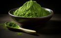 Een stapel heldergroene matcha poeder in een bruine kom, met een houten lepel ernaast.
