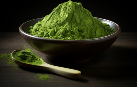 Een stapel heldergroene matcha poeder in een bruine kom, met een houten lepel ernaast.