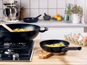 Zwarte wok en koekenpan met eten op een gasfornuis.