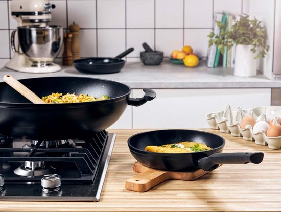 Zwarte wok en koekenpan met eten op een gasfornuis.