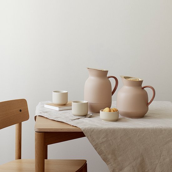 Deux carafes isothermes roses avec couvercles dorés et poignées marron sur une table avec deux tasses.