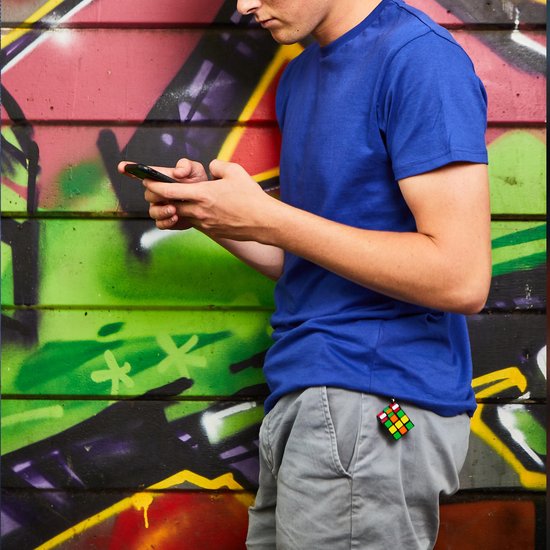 Rubik's Cube sleutelhanger aan de broekzak van een man in grijze broek en blauw T-shirt, tegen een graffiti muur.