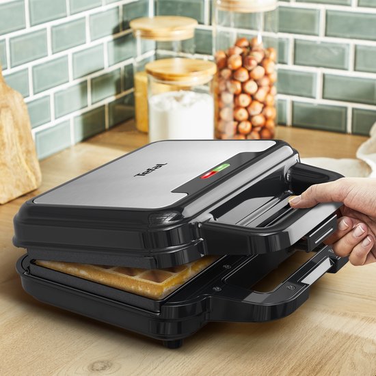 Hand opent zwart wafelijzer met een goudbruine wafel erin. Tefal logo zichtbaar.