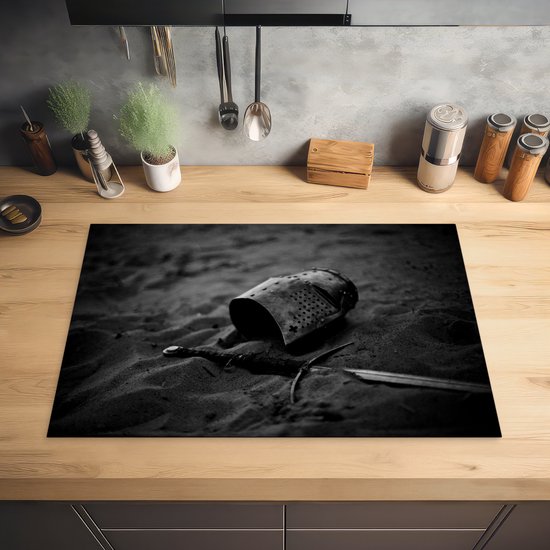 KitchenYeah® Inductie beschermer 76x51.5 cm - Een helm en zwaard uit de middeleeuwen liggen in het zand - zwart wit - Kookplaataccessoires - Afdekplaat voor kookplaat - Inductiebeschermer - Inductiemat - Inductieplaat mat