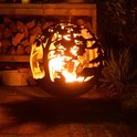 Roestbruine vuurschaal in bolvorm, verlicht door vuur, met open gesneden dieren en bomen.