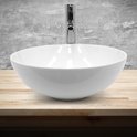 Lavabo rond blanc en céramique avec un robinet chromé sur une planche en bois devant un mur gris.