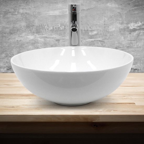 Lavabo rond blanc en céramique avec un robinet chromé sur une planche en bois devant un mur gris.
