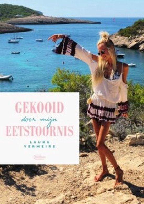 Een vrouw met lang blond haar, staand op een rotsachtige kust met de zee op de achtergrond. Ze draagt een witte, off-the-shoulder jurk met etnische franjes.