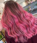 Vrouw met lang, golvend bruin haar met roze highlights.