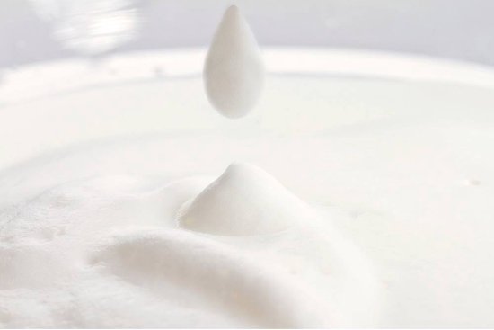 Een druppel melk valt in een bergje melkschuim.