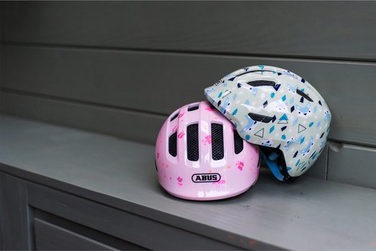 Lichtgroene kinderfietshelm met vossenpatroon en roze helm met bloemenpatroon naast elkaar.
