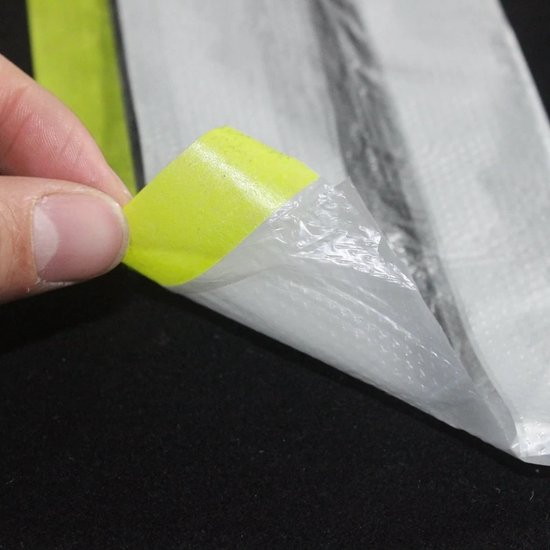 Hand met blauwe handschoen trekt gele tape van witte folie.