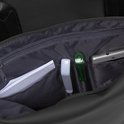 Binnenkant van een zwarte rugzak met open vakken. Een telefoon, documenten, een witte pen en een groene dispenser.
