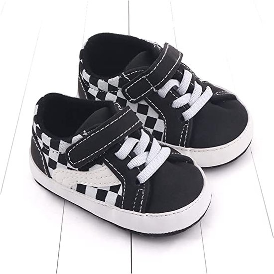 Babyschoentjes met zwart-wit dambordpatroon, klittenbandsluiting en witte veters. Wit met zwarte zolen.