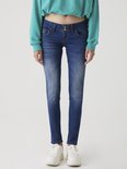 Model in blauwe jeans met knoopsluiting, gecombineerd met een groene trui.