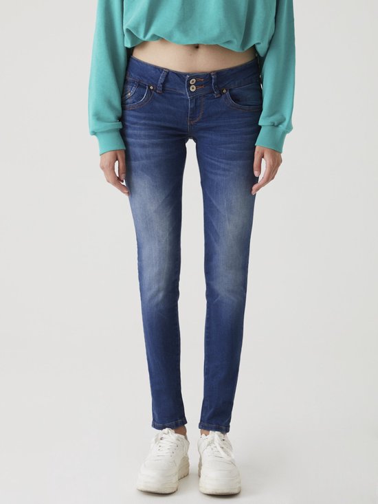 Model in blauwe jeans met knoopsluiting, gecombineerd met een groene trui.