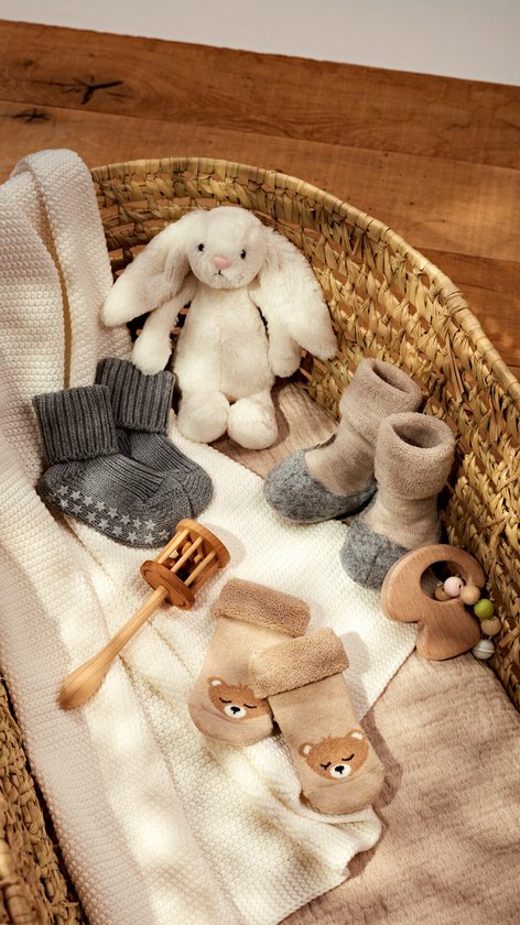 Wieg met babyproducten: konijntje, rammelaar, houten speelgoed en verschillende babysokjes in grijs, beige en naturel.