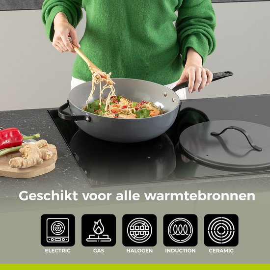 Grijze koekenpan met zwarte steel, waarin een vrouw noedels kookt. "Geschikt voor alle warmtebronnen" is zichtbaar.