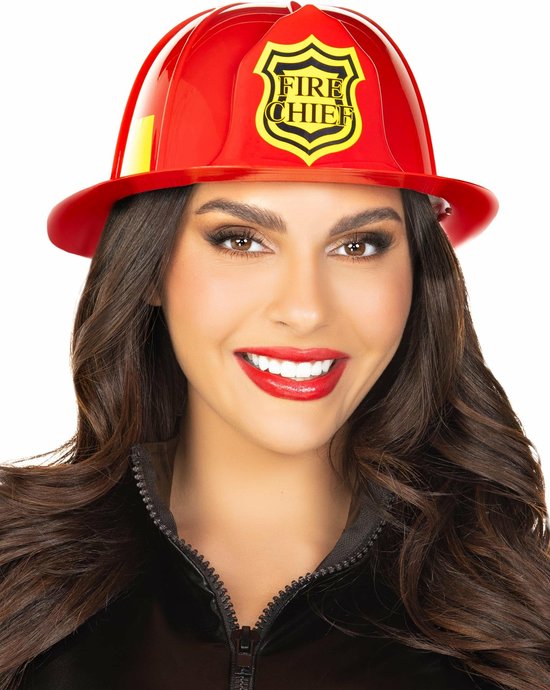 Vrouw met donker haar, draagt een rode brandweerhelm met 'FIRE CHIEF' embleem, en een zwarte jas.