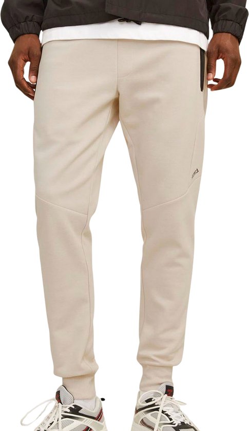 Close-up van een beige joggingbroek met zwarte ritszakken en logo.