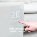 Een vinger bedient het touch display van een witte glazen convectorverwarming.