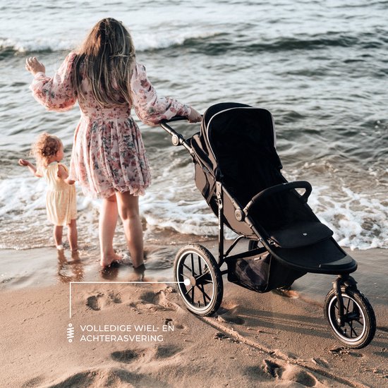Vrouw met een kind loopt op het strand met de zwarte driewielkinderwagen, golven op de achtergrond.