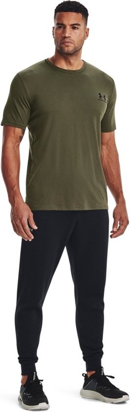 Man in groen Under Armour sportshirt met zwart logo, gedragen met zwarte trainingsbroek.