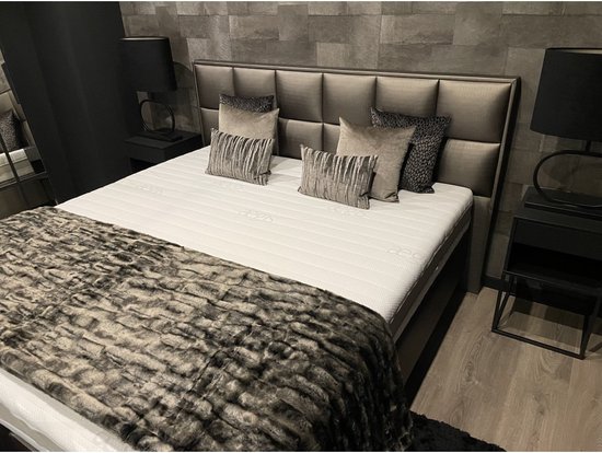Luxe bed met bruin gestoffeerde boxen, wit matras, grijs gestreept hoofdbord en een faux bont sprei.
