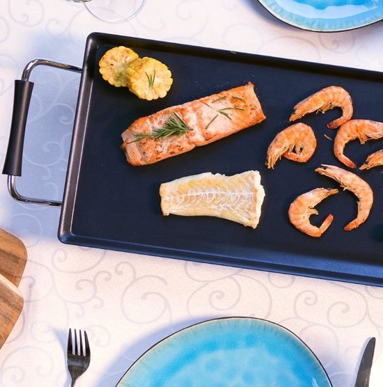 Gegrilde zalm, kabeljauw, maïs en garnalen op een zwarte bakplaat met een klassiek tafelkleed.