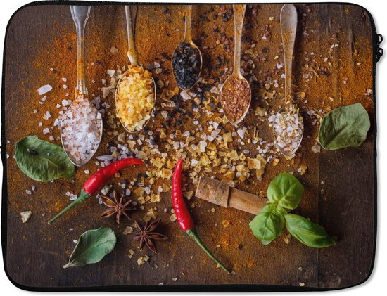 Housse d'ordinateur portable avec quatre cuillères remplies d'épices variées, y compris du sel, du poivre et des herbes. Deux piments rouges, de l'anis étoilé et des feuilles de basilic se trouvent parmi les épices.
