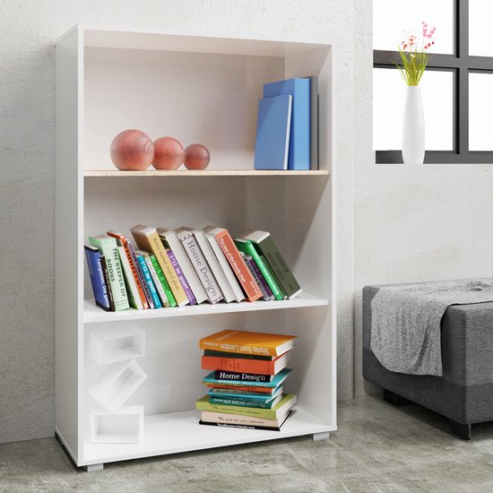 Witte boekenkast in een woonkamer met boeken, decoratieve ballen en een vaas met bloemen op de achtergrond.