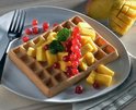 Gekleurde wafel op een bord, gegarneerd met mangoblokjes en rode bessen.