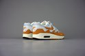 Achterkant van een witte met oranje Nike Air Max 1 Patta sneaker met beige zool en bruine hiel.
