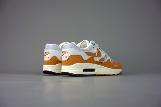 Achterkant van een witte met oranje Nike Air Max 1 Patta sneaker met beige zool en bruine hiel.