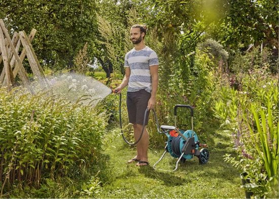 Man spuit water op planten met tuinslang uit een Gardena haspel in een groene tuin.