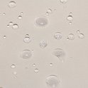 Textuuraanzicht van een lichtbeige, waterafstotend kussenmateriaal met waterdruppels.