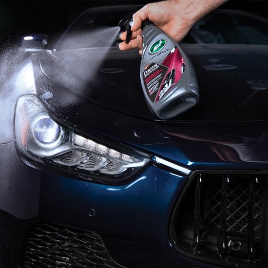 Main pulvérisant Turtle Wax Ceramic 3-en-1 Detailer sur le capot d'une voiture bleu foncé.