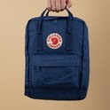Koninklijk blauwe Kånken rugzak met Fjällräven logo, vastgehouden door een hand.