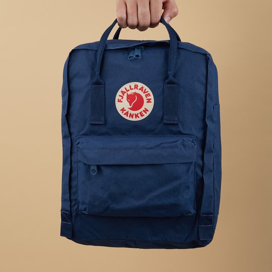 Koninklijk blauwe Kånken rugzak met Fjällräven logo, vastgehouden door een hand.