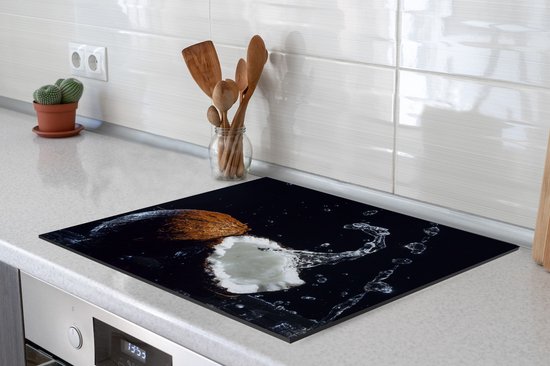 Een kokosnoot met waterplassen op een inductiebeschermer, geplaatst op een kookplaat.