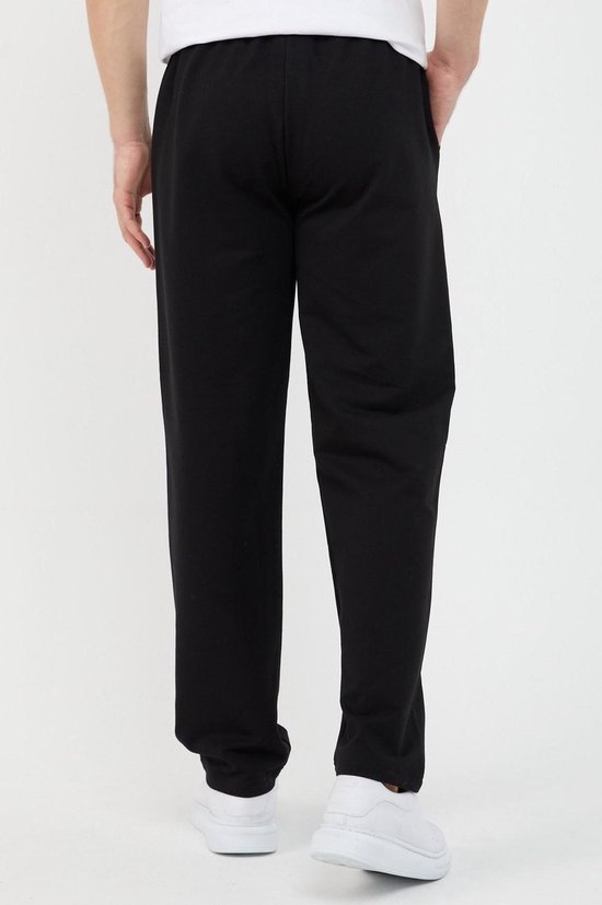Achterkant van een zwarte joggingbroek gedragen door een man met witte sneakers.
