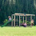 Speeltoestel met glijbaan, schommel, klimnet en monkey bars, met spelende kinderen.