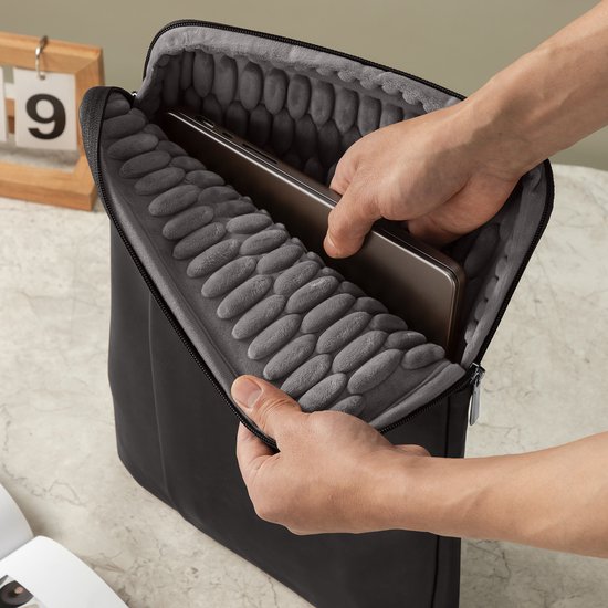 Handen plaatsen een laptop in een zwarte laptoptas met beschermende, noppen-achtige voering.