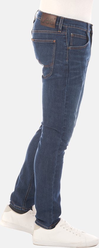 Zijaanzicht van een man in een donkerblauwe jeans met oranje stiksels en een bruin Lee-label.