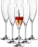 Zes glazen champagneglazen met verticale ribbels, één gevuld met roze drank, frambozen en takjes.
