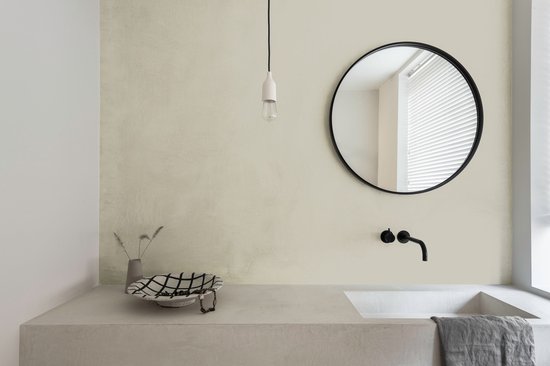 Badkamer met betonnen wastafel, ronde spiegel en zwarte kraan in lichte, egale muur.
