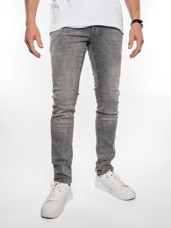 Man met grijze slim fit jeans, wit T-shirt en witte sneakers. De jeans heeft omgeslagen broekspijpen.