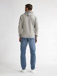 Achterkant van een man in een lichtgrijze hoodie en lichtblauwe jeans met witte sneakers.
