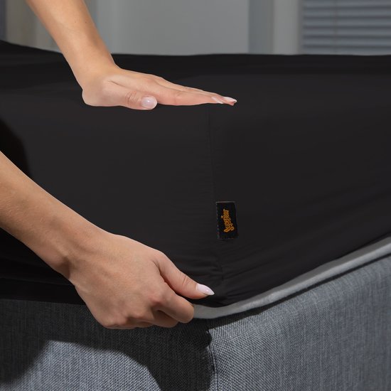 Handen leggen een zwart Superieur hoeslaken op een matras.